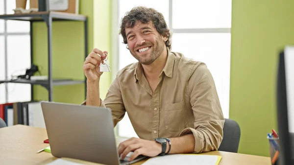 Young hispanic man real state agent holding key of new home working at office