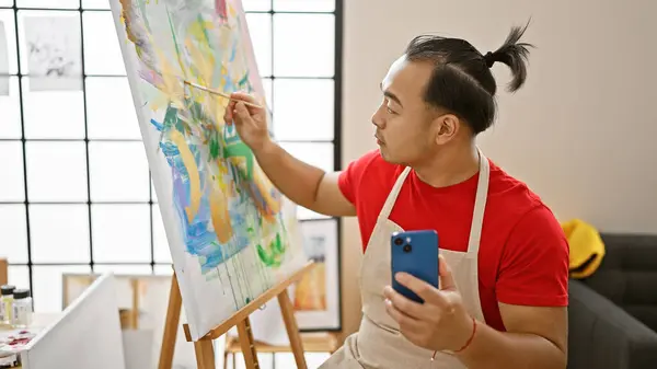 Young chinese artist immersed in drawing via smartphone, embracing tech creativity at art studio