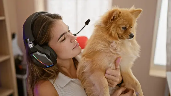 Gaming night with young hispanic streamer woman, headphones on, playing in dark, home gaming room. relaxed, yet serious, sharing her love for digital entertainment with her pet dog alongside.