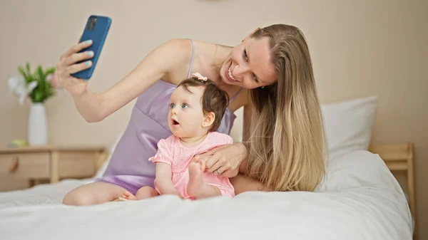 Mother and daughter having video call sitting on bed at bedroom
