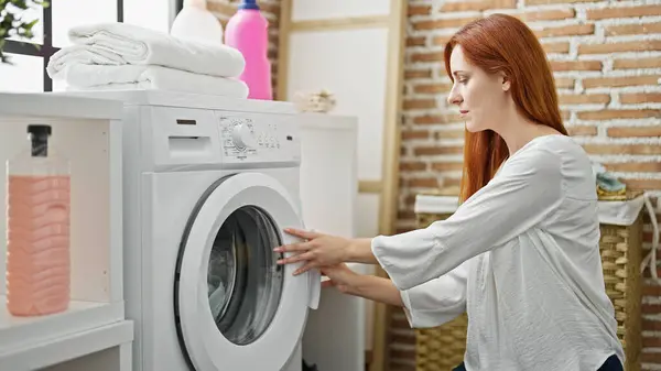 Young redhead woman washing clothes at laundry room