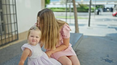 Kafkas anne ve kızı, neşe dolu, bir bankta birlikte oturuyorlar, hareketli bir sokakta sevgi dolu bir öpücük paylaşıyorlar.