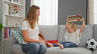 Beyaz bir anne ve kızın evde birlikte bir doğum günü hediyesi açması, sıcak gülümsemeleri odayı aydınlatıyor.