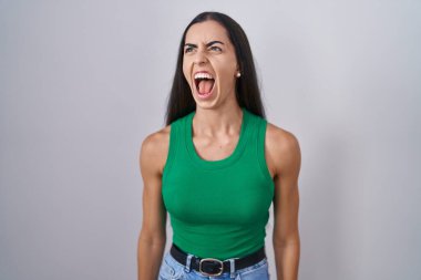 Young woman standing over isolated background angry and mad screaming frustrated and furious, shouting with anger. rage and aggressive concept. 