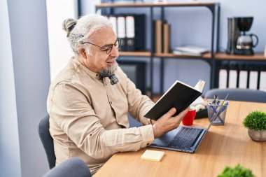 Middle age grey-haired man business worker using laptop reading book at office