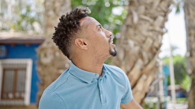 Parkta ciddi bir ifadeyle gökyüzüne bakan Afrikalı Amerikalı bir adam.