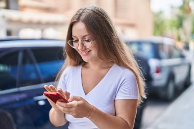 Sokakta akıllı telefon kullanan, kendine güvenen genç sarışın kadın.