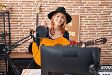 Genç beyaz kadın müzik stüdyosunda klasik gitar çalıyor. Gülümsüyor, mutlu bir şekilde işaret ediyor. 