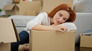 Genç kızıl saçlı kadın yeni evinde kendine güvenen bir paket tutuyor.