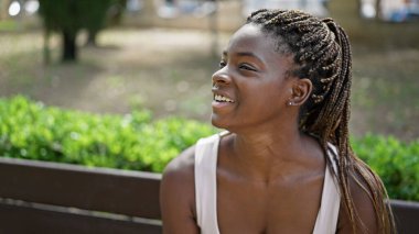 Afro-Amerikalı kadın yan tarafta oturuyor, parkta gülümsüyor.