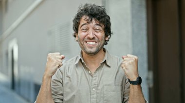 Genç İspanyol adam gülümsüyor. Kazanan jestle caddede duruyor.