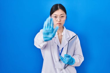 Laboratuvarda çalışan Çinli genç bir kadın avucunun içinde şarkı söylemeyi kesiyor. Yüzünde olumsuz ve ciddi bir jest olan uyarı ifadesi. 