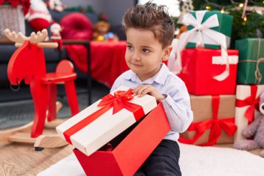 Tapılası İspanyol bebek evde Noel ağacının yanında oturmuş hediyesini açıyor.