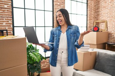 İspanyol kadın yeni evinde dizüstü bilgisayar kullanarak başarıyı mutlu bir gülümsemeyle ve kazanan ifadeyle kutluyor. 