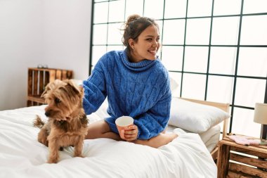 Genç, güzel, İspanyol bir kadın. Bir fincan kahve içiyor. Yatakta köpekle oturuyor.