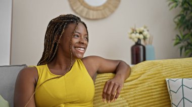 Afro-amerikalı bir kadın evdeki koltukta kendinden emin bir şekilde oturuyor.