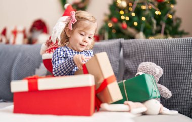 Sevimli İspanyol kız elinde hediyeyle evdeki Noel ağacının yanındaki koltukta oturuyor.