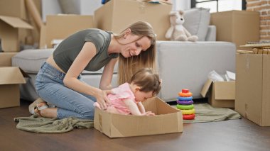 Anne ve kızı yeni evlerinde yerde oturup basketbol oyuncağıyla oynuyorlar.