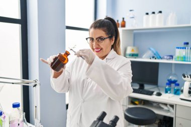 Young beautiful plus size woman scientist putting plant with tweezers on bottle at pharmacy