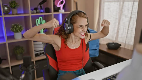 Joyful young woman streamer confidently playing video game, boasting winner smile in the dimly lit gaming room at home! perfect blend of technology and entertainment.