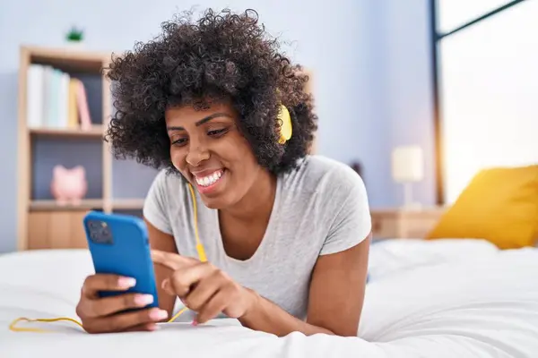 African american woman listening to music lying on bed at bedroom