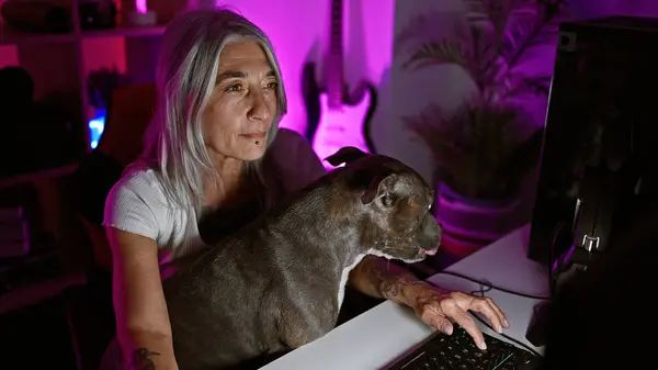 Fierce focus, grey-haired middle age woman streamer seriously playing games on stream, dog by her side in cozy gaming room