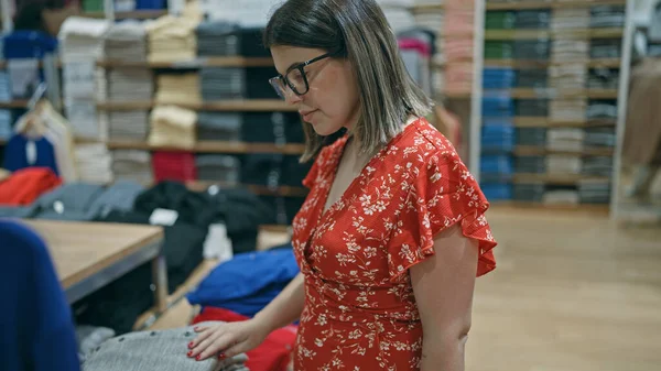 Moda tutkusu! Gözlüklü güzel İspanyol kadın perakende mağazasından şık kıyafetler seçiyor. Alışveriş merkezindeki bir butikten alışveriş yapan esmer bir kızın portresi..