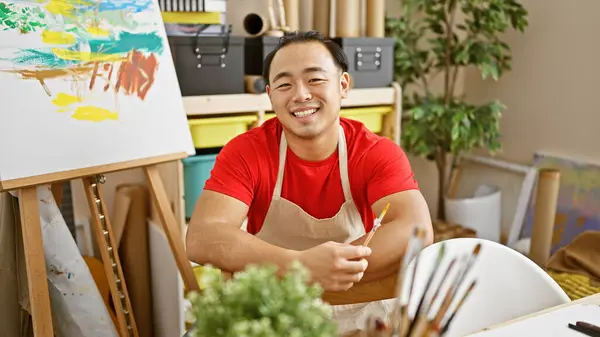 Vibrant snapshot, confident young chinese artist, brush in hand, flashing a happy smile, and mastering his craft, sitting in the heart of an indoor art studio