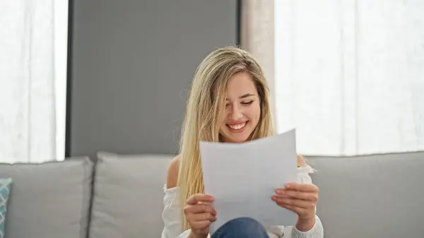 Young Blonde Woman Reading Document Sitting Sofa Home — Stok fotoğraf
