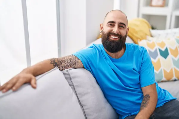 Young bald man smiling confident sitting on sofa at home