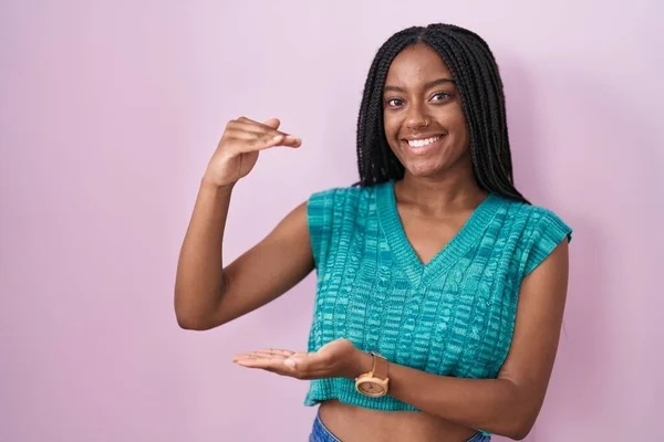 年轻的非洲裔美国人 头戴辫子 站在粉色背景上 手握大而大的标志 测量符号 微笑着看着摄像机 计量概念 — 图库照片