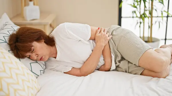 Middle age woman suffering for stomach ache lying on bed at bedroom