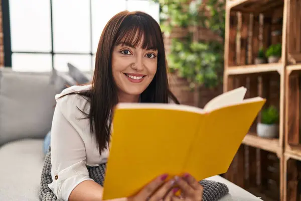 stock image Young beautiful hispanic woman reading book lying on sofa at home