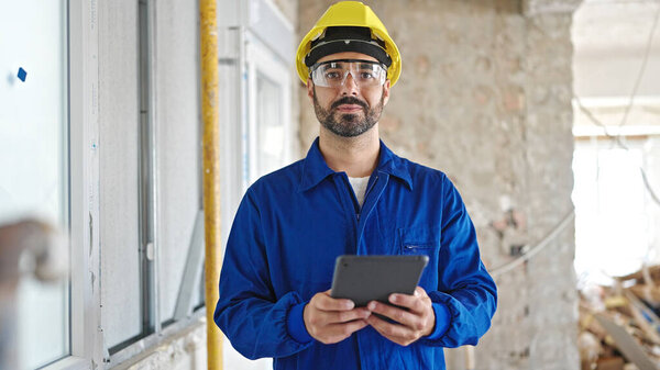 Young hispanic man worker wearing hardhat using touchpad at construction site