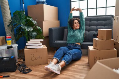 Genç, güzel, İspanyol bir kadın yeni evinde yerde oturmuş kollarını açıyor.