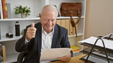 Mutlu kıdemli bir adam iş belgesini okurken özgüvenle el hareketi yapıyor. Olgun bir yönetici olarak iş yerinde başarısını kanıtlıyor..