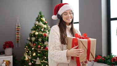 Genç, güzel, İspanyol bir kadın Noel ağacının yanında elinde hediyesiyle dans ediyor.