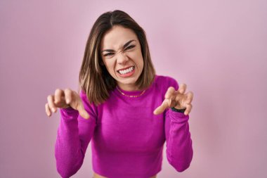 İspanyol kadın pembe arka planda durup gülümsüyor. Pençe hareketini kedi gibi yapıyor. Agresif ve seksi bir ifade. 