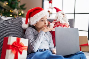 Sevimli Çinli kız evdeki Noel ağacının yanında kanepede otururken görüntülü konuşma yapıyor.