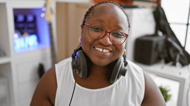 Kendinden emin Afrikalı Amerikalı kadın müzisyen, neşe saçıyor, müzik stüdyosunda kulaklık takıyor.