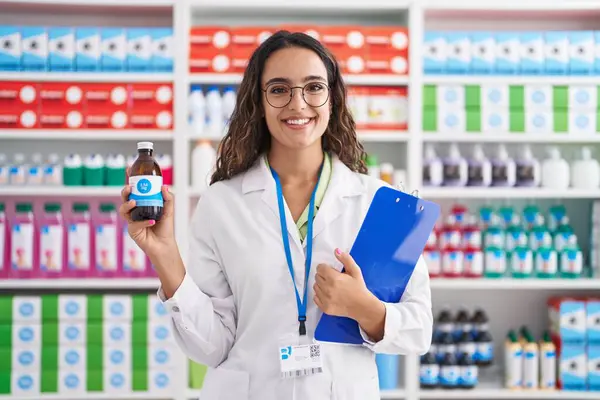 Young hispanic woman working at pharmacy drugstore holding syrup smiling with a happy and cool smile on face. showing teeth.