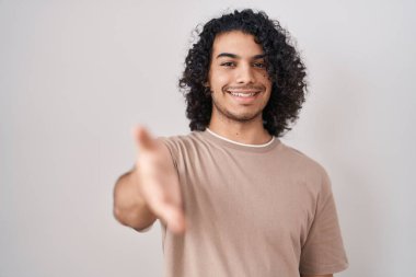 Beyaz arka planda duran kıvırcık saçlı İspanyol bir adam dostça bir selamlama ve hoş geldin hediyesi olarak el sıkışma teklif ediyor. başarılı iş. 