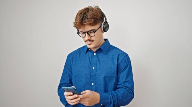 Genç İspanyol adam, izole edilmiş beyaz arka plan üzerine kulaklık takarak akıllı telefon kullanıyor.