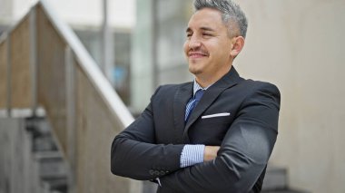 Genç İspanyol iş adamı gülümsüyor. Kendine güveni tam. Sokakta çapraz hareketlerle duruyor.