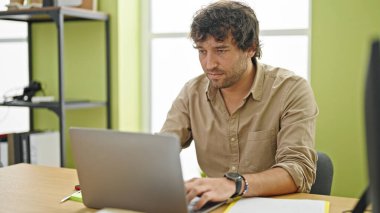 Genç İspanyol iş adamı ofiste ciddi suratlı dizüstü bilgisayar kullanıyor.