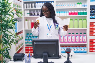 Afrika kökenli Amerikalı kadın eczacı elinde ilaç şişesiyle eczanede reçete okuyor.