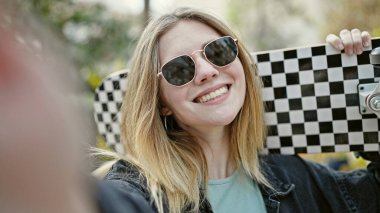 Sarışın genç bir kadın parka gülümseyen bir kamerayla selfie çekiyor.