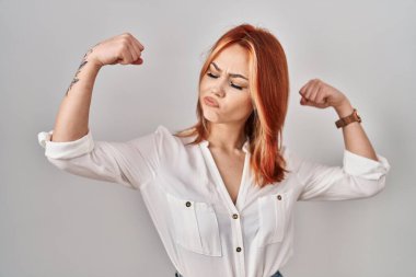 Young caucasian woman standing over isolated background showing arms muscles smiling proud. fitness concept. 