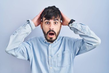 Mavi arka planda sakallı genç İspanyol bir adam var. Deli ve korkmuş, elleri başında, ağzı açık ve şoktan korkmuş ve şaşırmış. 