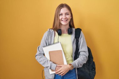 Öğrenci çantası takan, elinde kitaplarla kameraya seksi bir ifadeyle bakan beyaz bir kadın. Neşeli ve mutlu bir yüz.. 